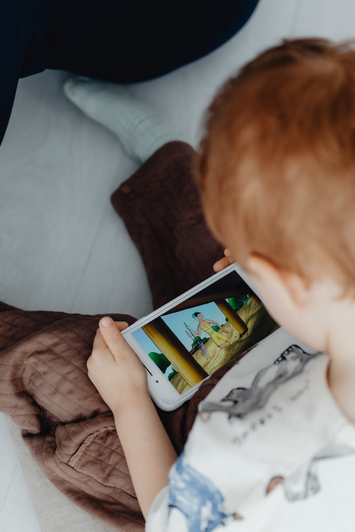 Young boy watching cartoons on a tablet indoors, focusing on leisure and entertainment.